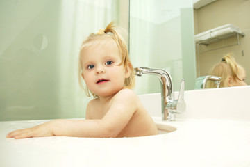 Cute blonde baby taking bath in bathroom sink	