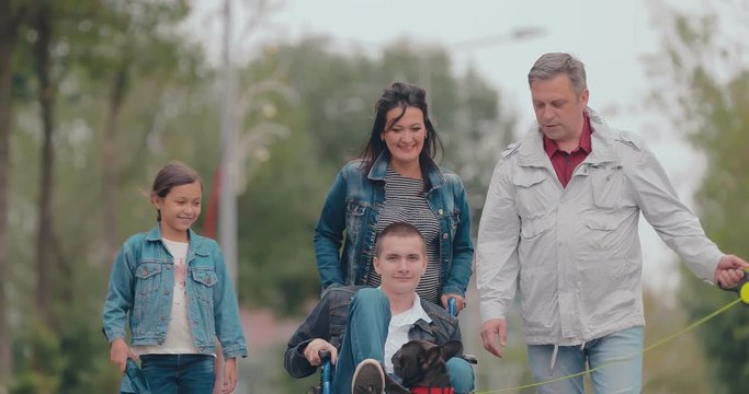 Dog playing with a guy in a wheelchair. Friendly family spends the day together, a teenager with disabilities.
