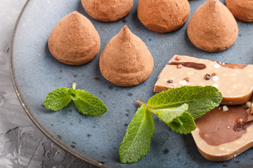 Chocolate truffle with piece of milk chocolate on blue ceramic plate on gray concrete background.