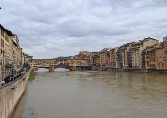 Obraz premium View of the Ponte Vecco bridge, ancient buildings and the Arno River in Florence on an overcast day.