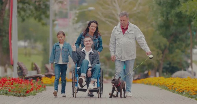 Happy family spends the day together for a walk in the park. Young man with disabilities walks with his parents, sister and dog.