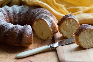 The round sweet cake strewed with icing sugar on a wooden board with a knife. 