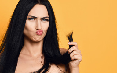 Obraz premium Frustrated brunette woman examining dry damaged hair over yellow