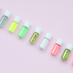 Colorful glitters lies on pastel pink background. Many round jars with multi-colored bright sparkles for nail polish