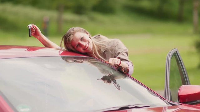 Excited young blonde woman admires her red glistening new car