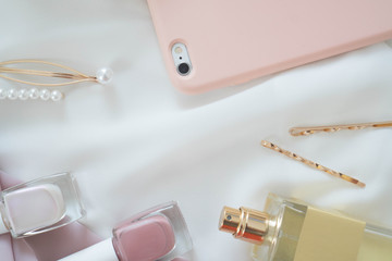 Flat composition of nail polish, bottle of perfume, gold hairpins with pearls and smartphone in peach color case. Accessories of fashionable, modern, self-confident girl, a fashion, beauty blogger