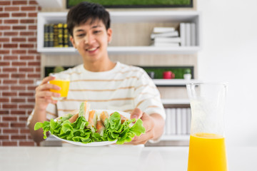 A young Asian man holding a plate of vegetable snack roll and a glass of orange juice.