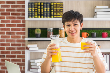 A smiling young Asian man holding a jar and a glass of orange juice.