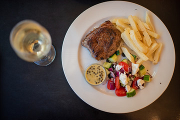 Steak and chips with salad and a glass of white wine shot from directly above