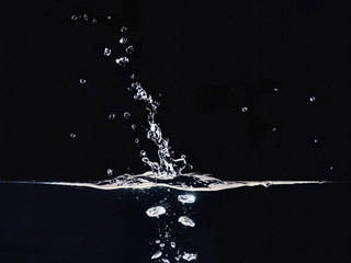 Droplet of water photographed while making splash on liquid surface, isolated on black background,...