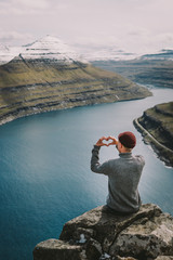 Naklejka premium Man on top of mountain shows heart Faroe islands