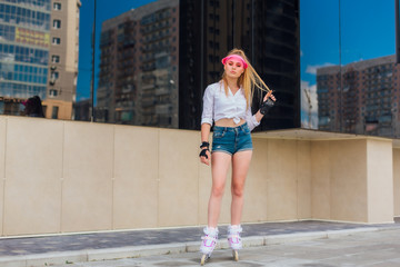 Portrait of an emotional girl in a pink cap visor and protective gloves for rollerblades and skateboarding riding on rollerblades on the road.