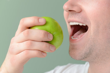 Man with healthy teeth and apple on color background, closeup