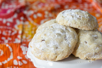 Stack of Russian Tea Cake cookies on a white cake plate on a bright summer fabric of orange, red, yellow, pink, and white