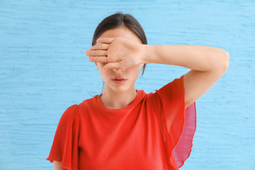 Young woman covering her eyes on color background