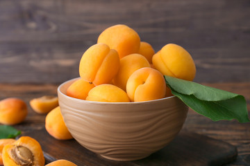 Bowl with tasty ripe apricots on wooden table