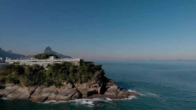Aerial view of small island with recreational construction on top at the coast of Rio de Janeiro revealing the famous peaks of the city such as Corcovado and Two Brothers mountain in the background