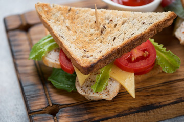 Sandwich with chicken, cheese, salad leaves and tomatoes on a wooden serving board, close-up, studio shot