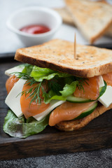 Sandwich with salmon, cheese, salad leaves and cucumber, selective focus, closeup, vertical shot