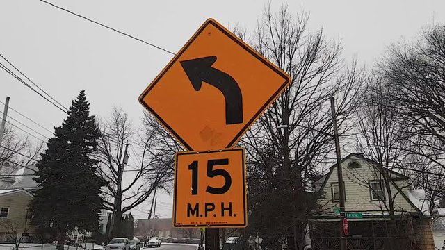 Shot Walking Away Of An Orange Turn Left Traffic Sign With Recommended Speed Limit In New York On A Winter Snowy Day - Snow And Cold - 1080p 240fps