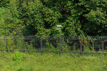Surveillance camera on a metal fence with barbed wire.