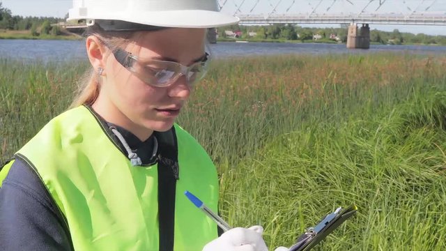 The ecologist carries out a visual express analysis of water in a reservoir and river. The data of the inspection of the coastal territory and the results of the analysis are recorded.