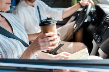 cropped view of woman sitting in car and holding paper cup near driver