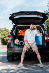 handsome bearded man standing near car and touching cap