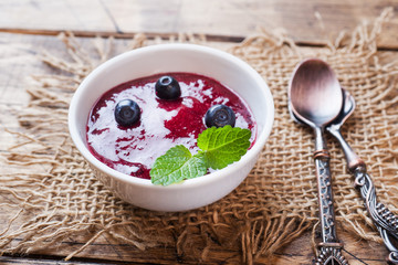 Blueberry jam in a plate and fresh blueberries on a wooden table.