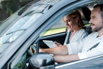 selective focus of man driving car while woman holding digital tablet