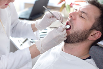 Profilaktyczny przegląd stanu uzębienia u mężczyzny w średnim wieku. Szeroko otwarte usta. W dłoniach lekarza ekskawator i lusterko dentystyczne.