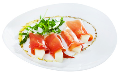 Tasty dish rolls of prosciutto di parma with melon served with arugula at plate