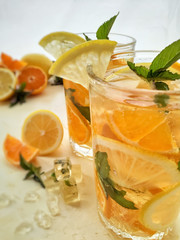 tea with lemon and mint. Refreshing drink with orange, lemon slices and mint leaves in a transparent glass close-up on a light background. Lemonade with citrus.