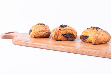 Three freshly baked puff pastry rolls filled with chocolate on a wooden board