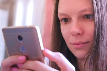 Young woman is reading a book on smartphone. She is looking at screen moving her eyes. Portrait of brunette girl online browsing and surfing web internet pages.