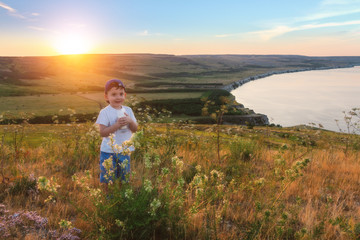 Happy childhood. Cheerful kid is drinking milk at the nature. Scenic view of the meadows, hills and the sea.