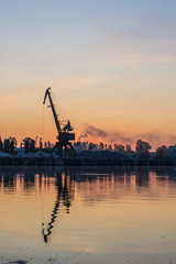 Fototapeta na wymiar Sunrise over the port. Dawn over the river. The cranes in the industrial part of the city on the shore.