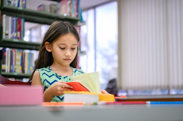 Cute little girl reading books in library attentively at school. Girl concentrating to learning by herself outside classroom. Education and People lifestyles. Academic and Kids duty concept.