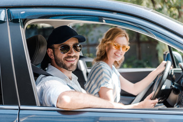selective focus of happy man in sunglasses smiling near attractive woman driving car