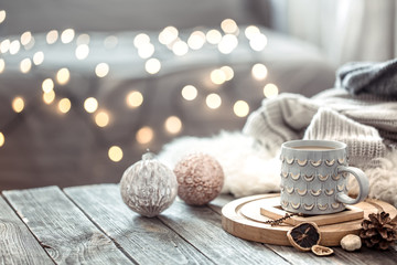 Coffee cup over Christmas lights bokeh in home on wooden table with sweater on a background and...