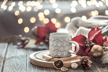 Coffee cup over Christmas lights bokeh in home on wooden table with flowers on a background and decorations. Holiday decoration, magic Christmas