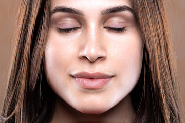 Fototapeta premium A closeup and front portrait of a stunning brunette girl with her eyes shut. Flawless skin complexion and minimal makeup.