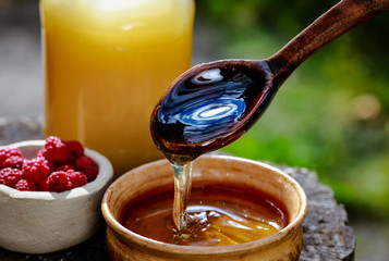 fresh sweet honey dripping in a wooden spoon in a ceramic bowl