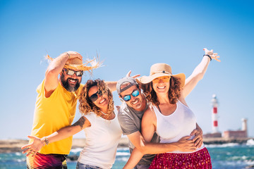 Group of happy people and cheerful adults friends have fun together during summer holiday vacation at the beach - enjoying the beach and ocean outdoor - blue sky and lighthouse in background