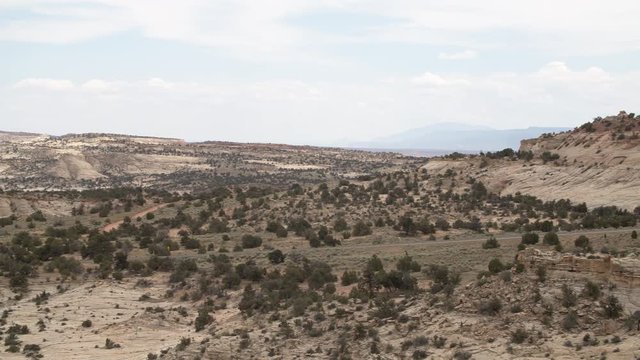 A wide panning shot of the Grand Staircase Escalante National Monument in Utah. In the distance a road can be seen with cars, giving a sense of scale.