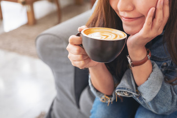Closeup image of a beautiful asian woman holding and drinking hot coffee in cafe