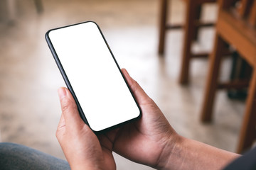 Mockup image of a woman holding black mobile phone with blank desktop screen while sitting in cafe