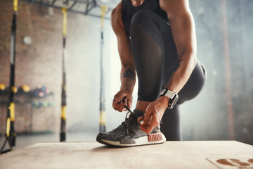 Preparing for workout. Cropped photo of beautiful young woman in sports clothing tying her shoelaces while exercising in gym.