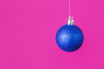 A bright New Year concept - a blue Christmas tree ball hanging on a pink background. Place for text, minimalism.