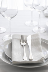 Table setting white and grey colour. Empty glasses and plates set with napkin and cutlery. Restaurant interior background...